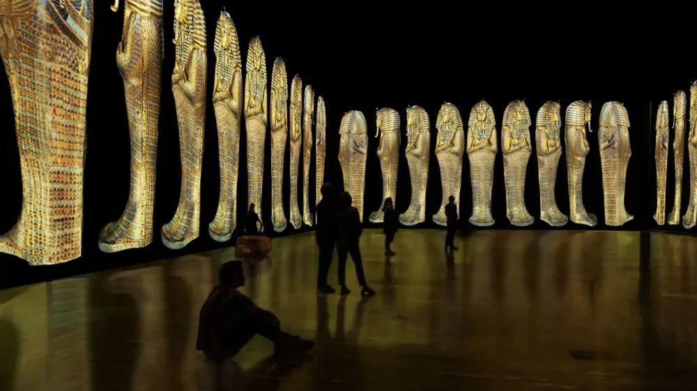 Images from inside the Beyond King Tut: The Immersive Experience, showing silhouettes of people looking at projections of sarcophagi lining the walls